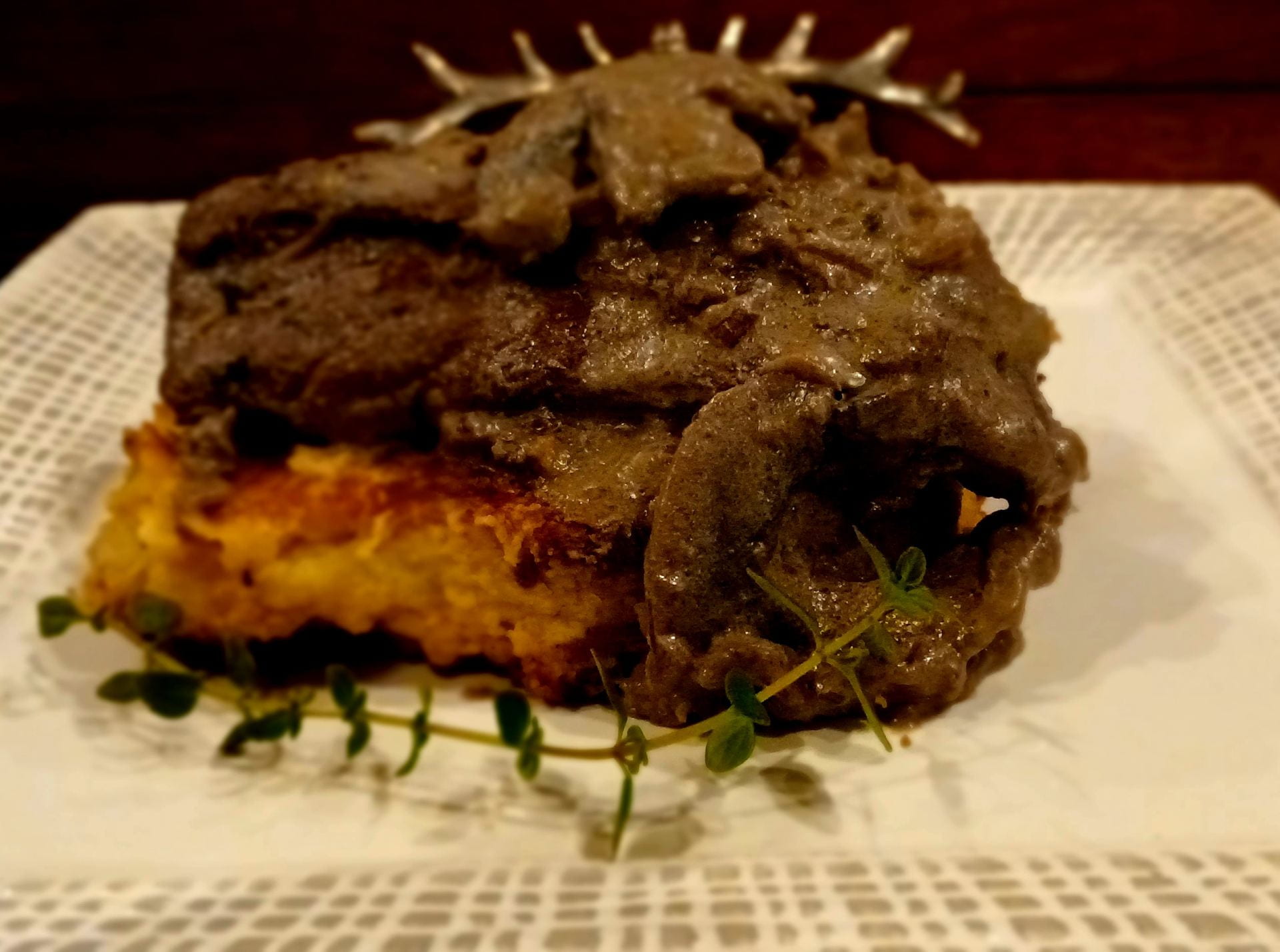 plated pan-seared tenderloin on top of a potato pancake with a mushroom sauce and sprig of thyme